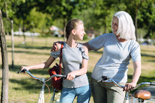 Family relationships. Joyful positive nice woman hugging her granddaughter and smiling while riding bikes together with her
