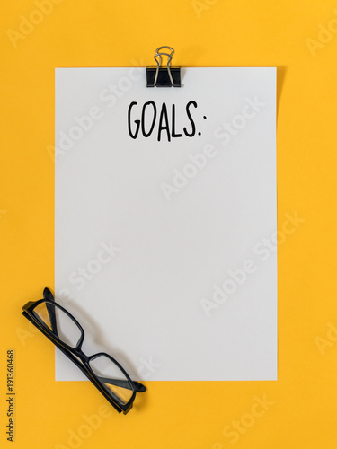 Top view goals list with notebook, glasses on yellow background with blank space for text. Flat lay. Copy space.