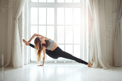 Young skinny woman doing yoga against window