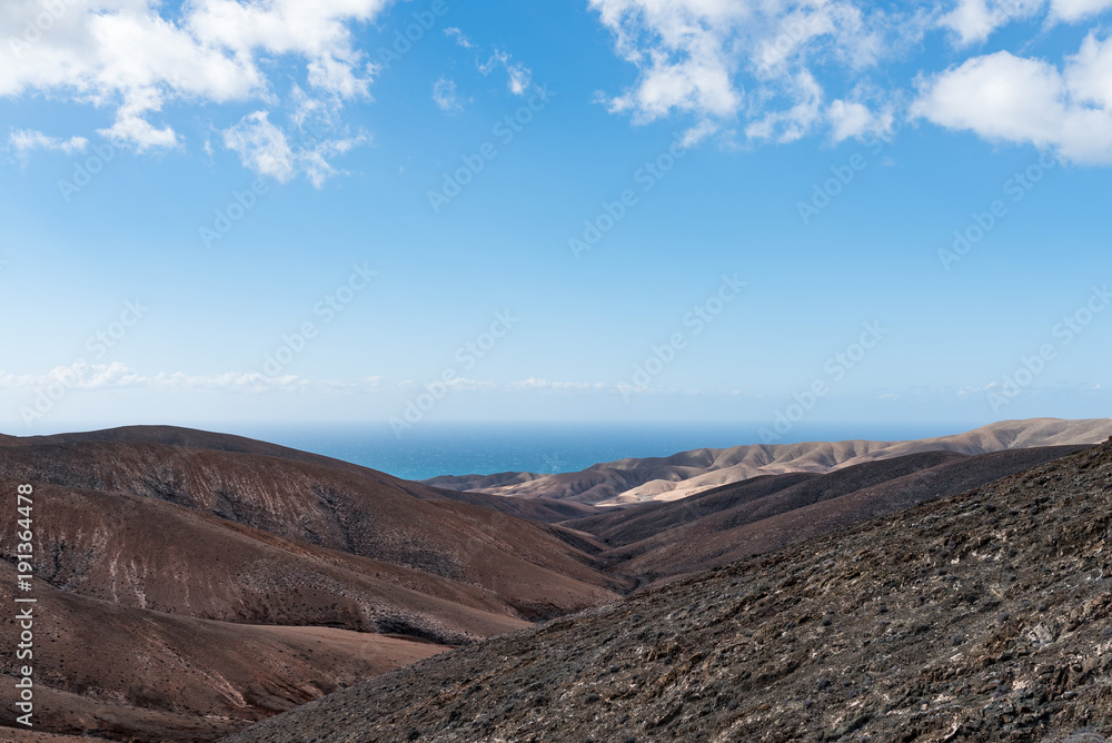 arid rolling landscape with ocean in background under blue sky on Fuerteventura island