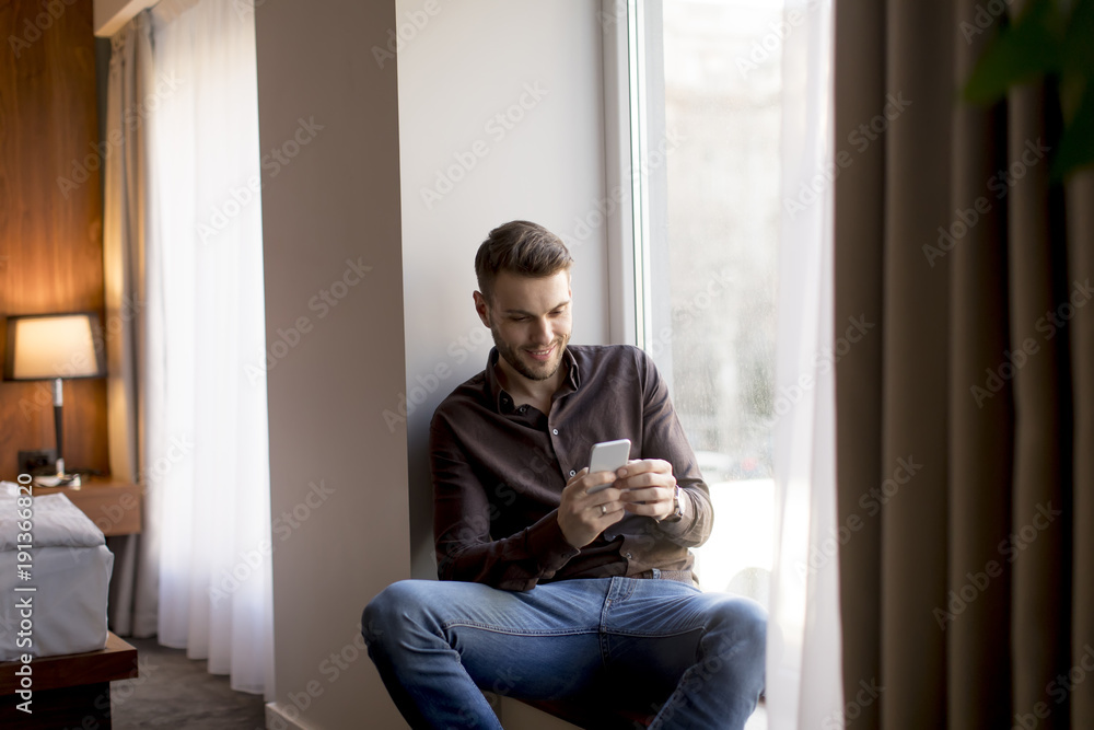Young businessman with mobile phone by window
