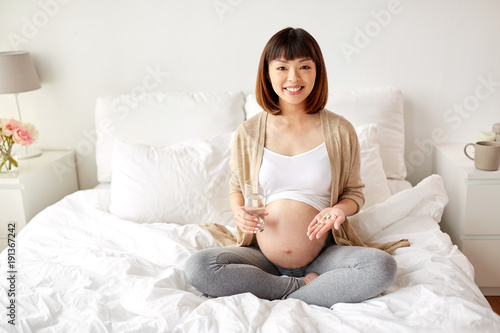 happy pregnant woman with pills in bed at home