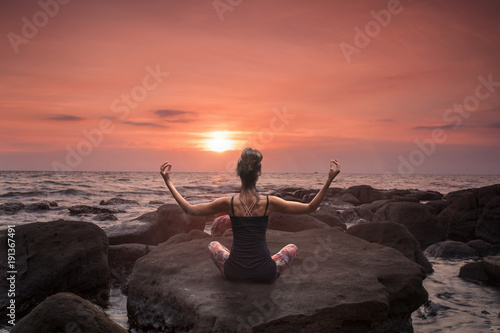 Frau meditiert auf einem Stein am Strand beim Sonnenuntergang