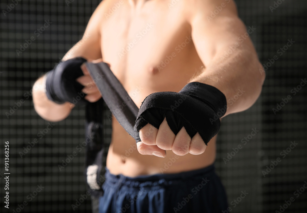 Fototapeta premium Young boxer applying wrist wraps in gym, closeup