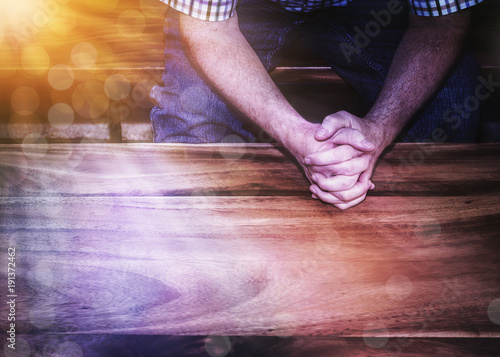 A man hands pray over wooden table with Bokeh light effected, copy space