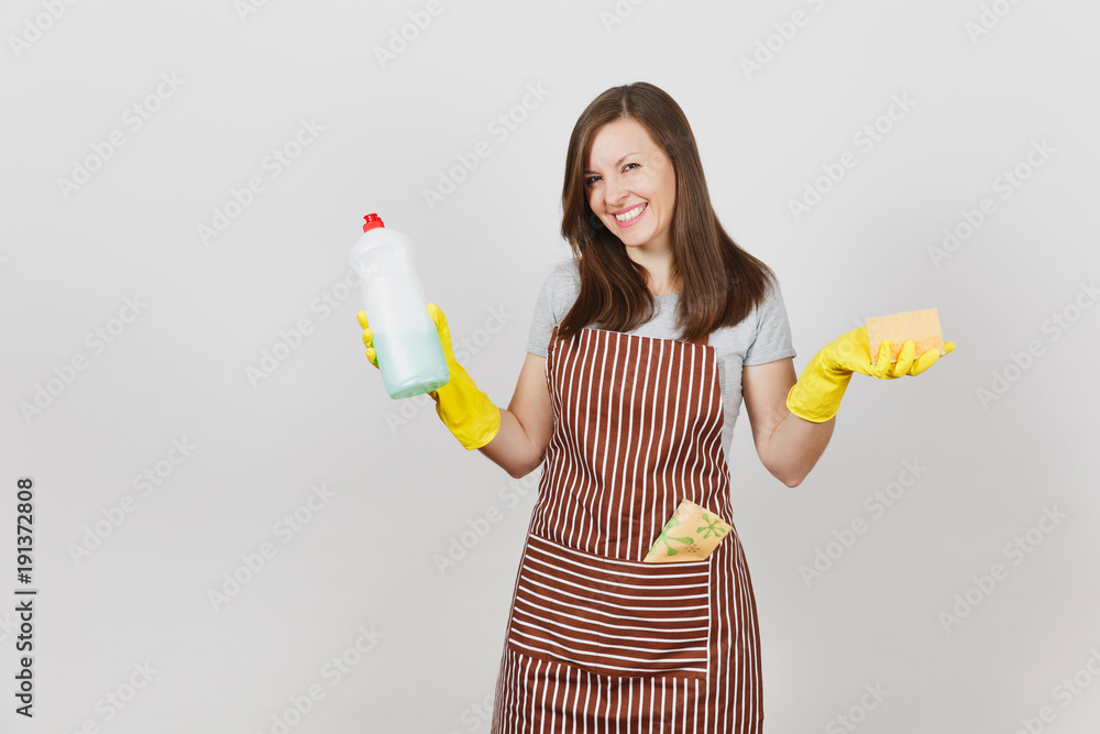 Young housewife in yellow gloves, striped apron, cleaning rag in pocket isolated on white background. Woman holding bottle with cleaner liquid for washing dishes, sponge. Copy space for advertisement. Young housewife in yellow gloves, striped apron, cleaning rag in pocket isolated on white background. Woman holding bottle with cleaner liquid for washing dishes, sponge. Copy space for advertisement.