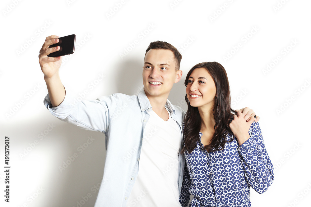 Beautiful excited young straight couple making funny faces, laughing, smiling & taking selfie, having fun w/ mobile cell phone camera gadget. Portrait, copy space, isolated white wall background. Beautiful excited young straight couple making funny faces, laughing, smiling & taking selfie, having fun w/ mobile cell phone camera gadget. Portrait, copy space, isolated white wall background.