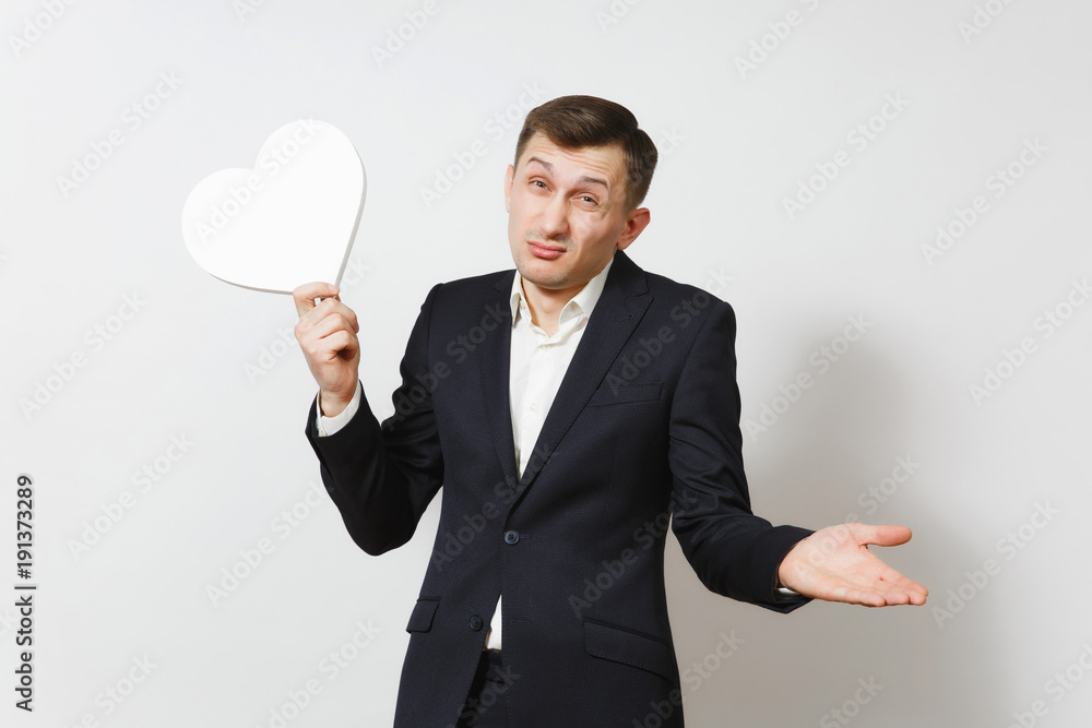 Young stunned shocked upset sad man in suit holding big white heart isolated on white background. Copy space for advertisement. St. Valentine's Day, International Women's Day, birthday holiday concept Young stunned shocked upset sad man in suit holding big white heart isolated on white background. Copy space for advertisement. St. Valentine's Day, International Women's Day, birthday holiday concept