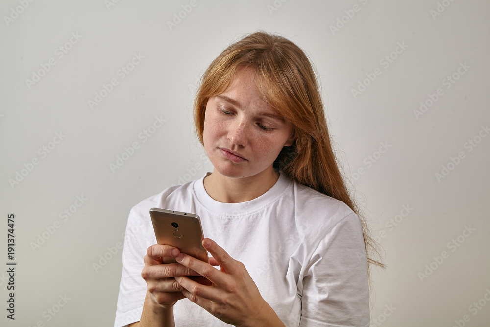 Headshot of young red-headed girl with freckles holding her phone in her hands and looking onto it as if reading her feed or text messages Headshot of young red-headed girl with freckles holding her phone in her hands and looking onto it as if reading her feed or text messages
