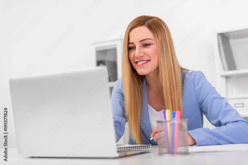 Beautiful young woman looks at the laptop monitor screen while sitting at the office desk. Beautiful young woman looks at the laptop monitor screen while sitting at the office desk.