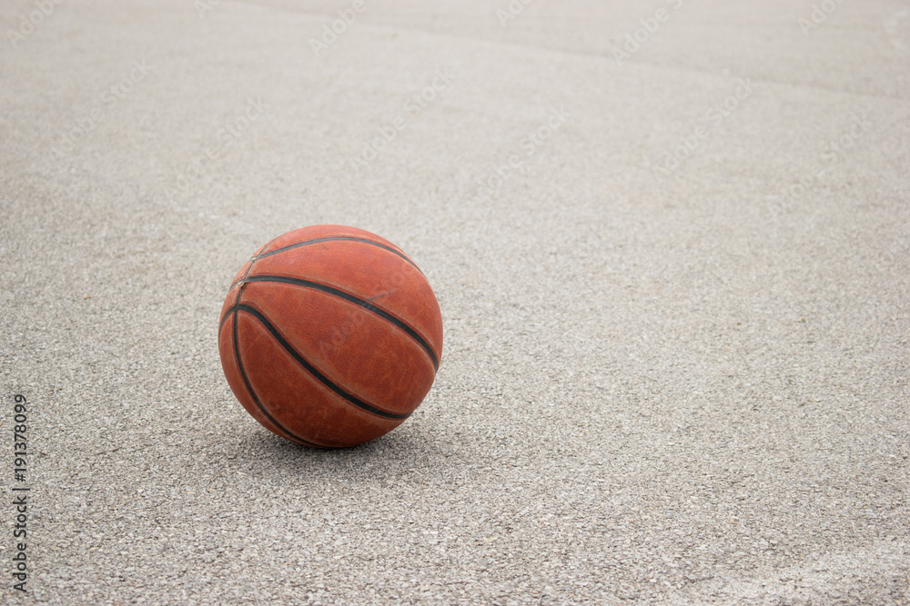 Used orange leather basketball on grey asphalt background.