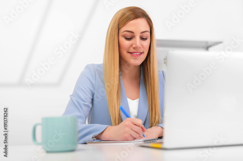 Attractive young woman working with documents and laptop in the workplace in a white office.