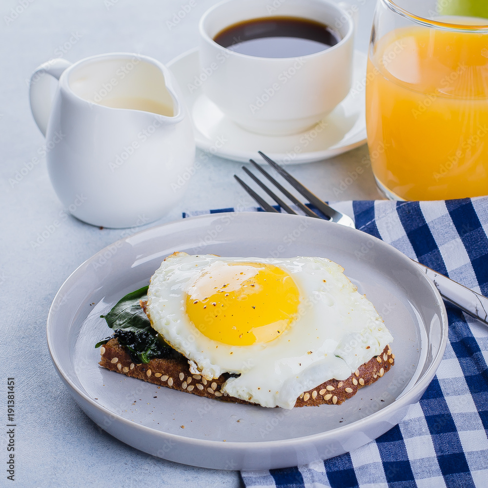 Fototapeta premium Rye bread toasts with fried spinach and egg with cup of coffee and orange juice on blue table background. Healthy Breakfast Food Concept.