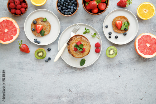 Breakfast table with pancakes, berries and fruits. Top view, gray light background
