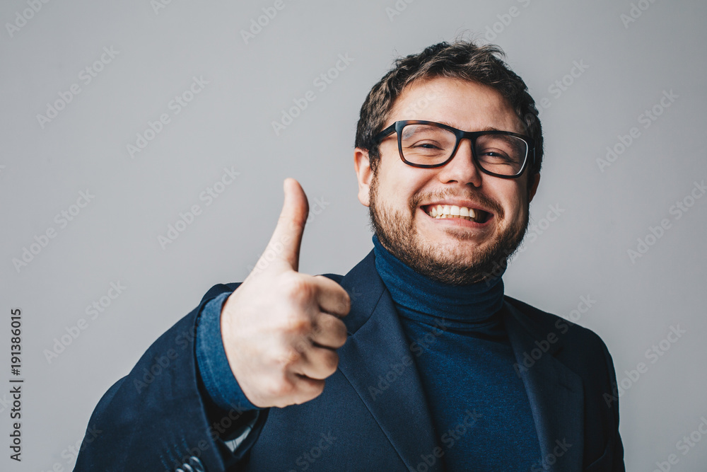 Happy young business man showing thumbs up gesture and smiling cheerfuly with white teeth. Isolated on grey background. Close up portrait Happy young business man showing thumbs up gesture and smiling cheerfuly with white teeth. Isolated on grey background. Close up portrait