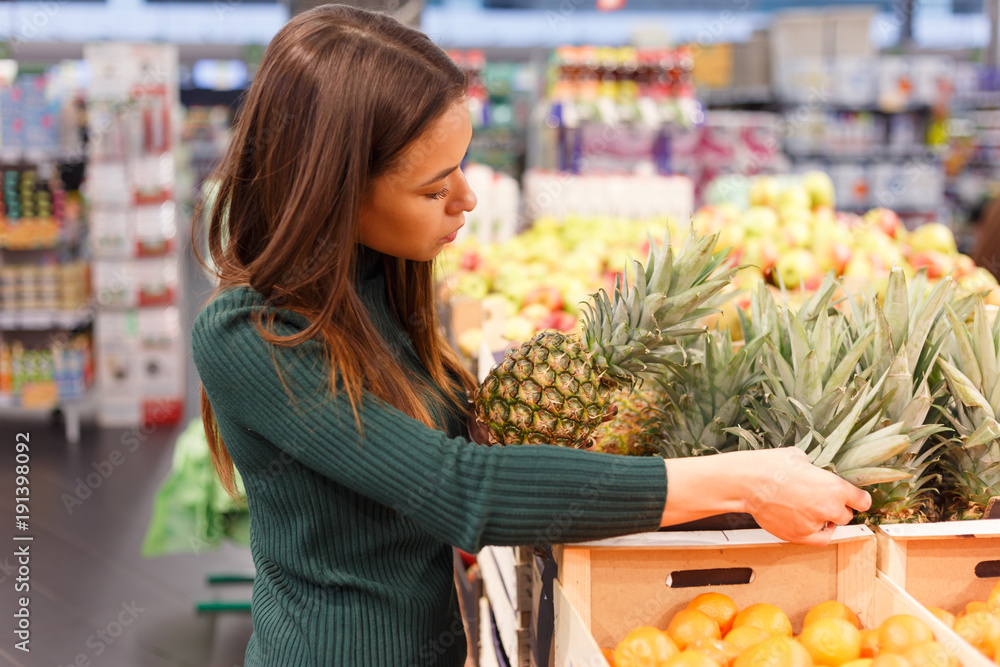 Fototapeta premium Young brunette woman buying pineapple at grocery shop.