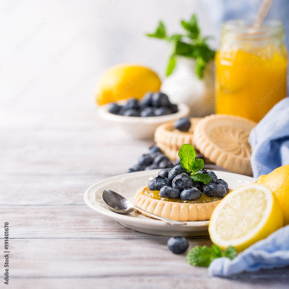 Shortbread homemade tartlet filled with lemon curd and fresh blueberries on rustic wooden background. Holiday food concept with copy space. Shortbread homemade tartlet filled with lemon curd and fresh blueberries on rustic wooden background. Holiday food concept with copy space.