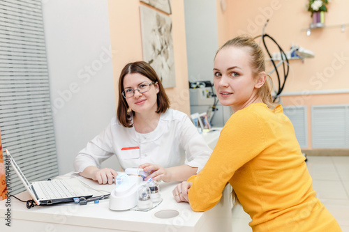 Woman doctor discussing diagnosis with her patient in cosmetology clinic, pointing at notebook screen
