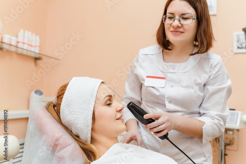 Beautiful woman getting modern facial darsonval therapy at the cosmetology clinic photo