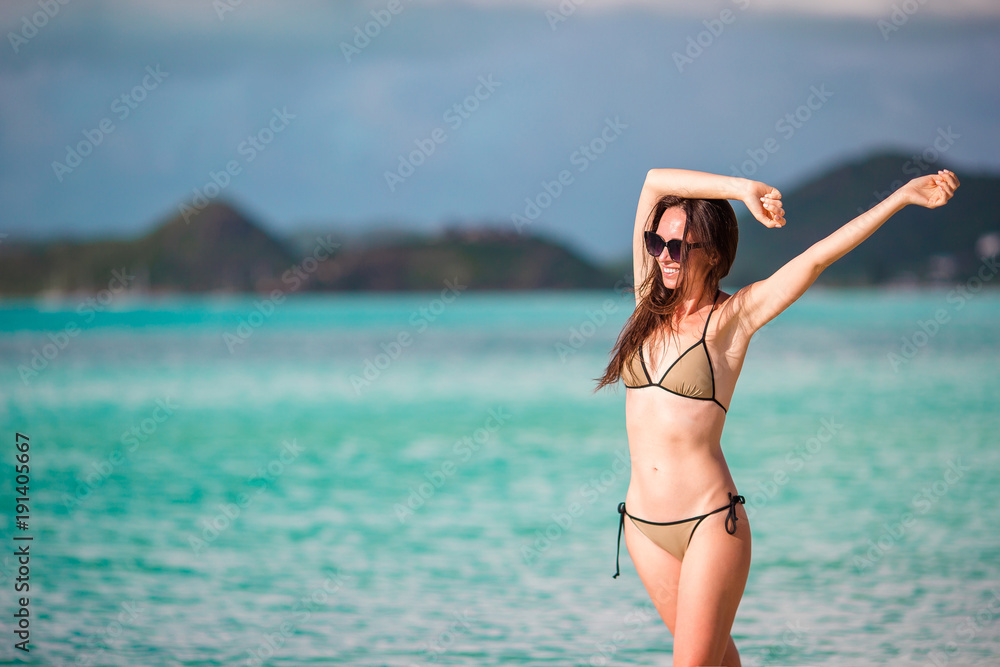 Beach vacation people - woman looking at perfect paradise with turquoise ocean water on caribbean vacation. Girl in bikini sunbathing on travel holidays on luxury island.