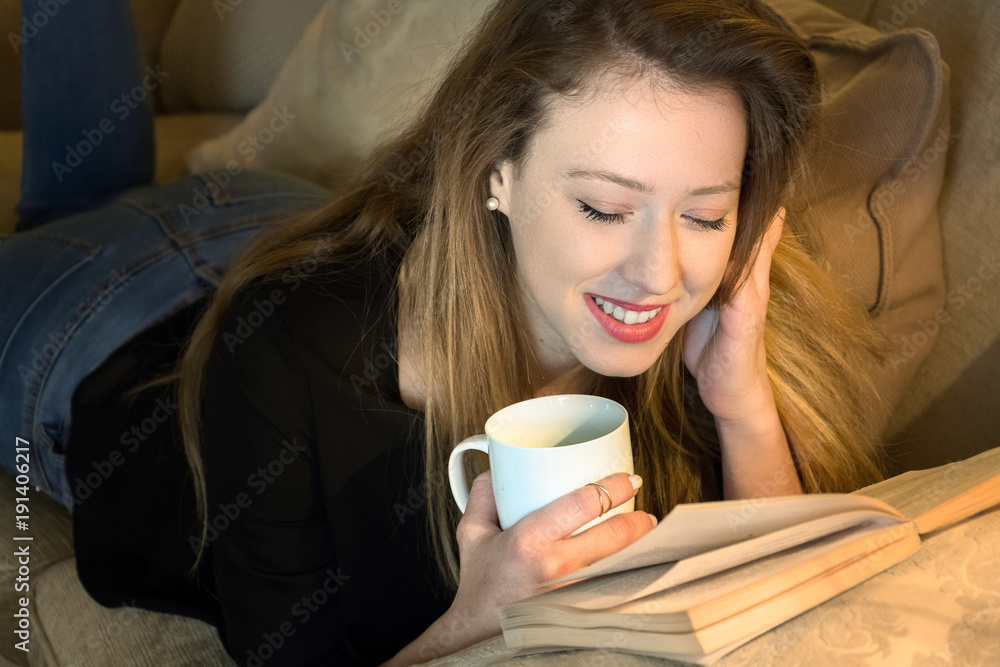Young woman lying face down reading a book and having coffee Young woman lying face down reading a book and having coffee