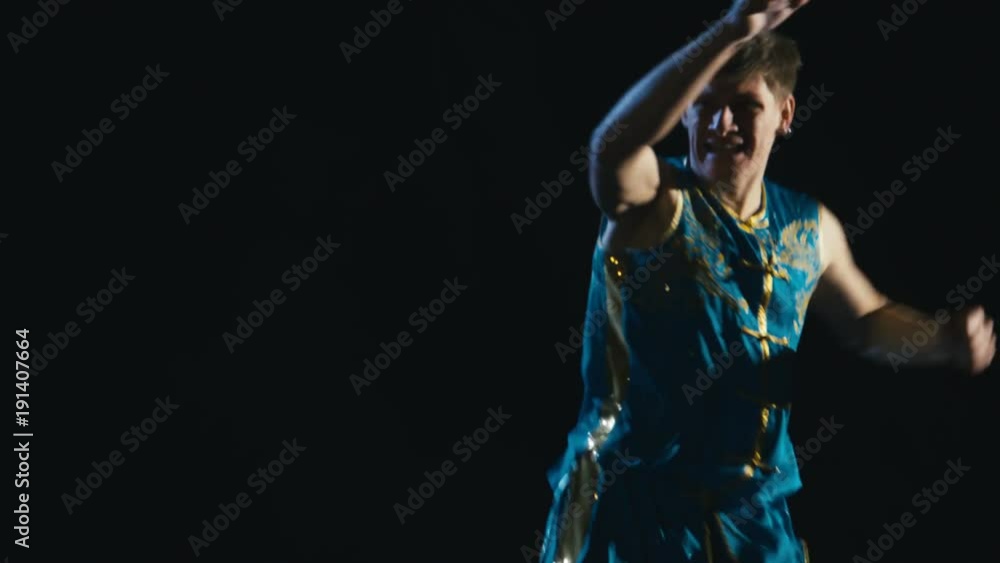 Young man training barehanded wushu against black background Young man training barehanded wushu against black background