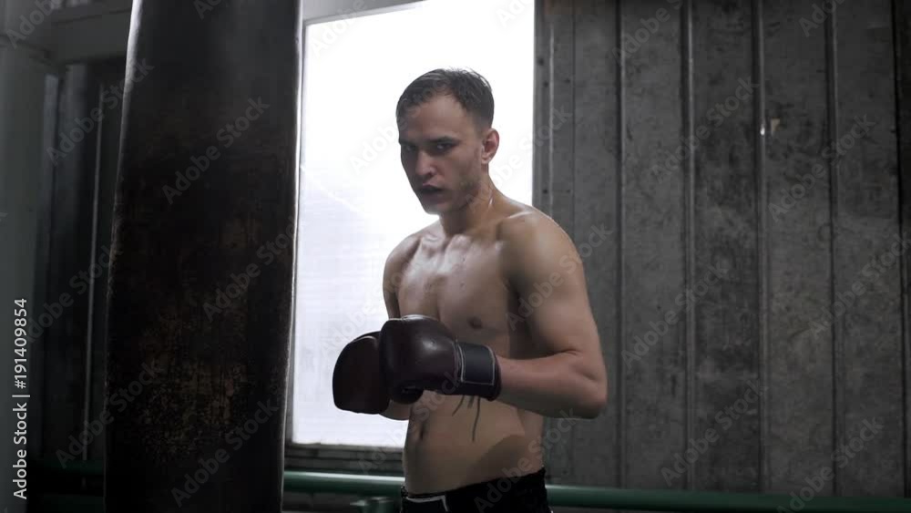 Portrait of tired sweaty boxer wearing sport shorts and boxing gloves breathing heavily after workout in gym, slow motion Portrait of tired sweaty boxer wearing sport shorts and boxing gloves breathing heavily after workout in gym, slow motion