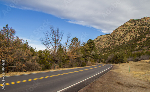 A highway disappearing around a curve between a rocky mountain dotted with shrubs and a stand of shrubs in a spring time american landscape © kat7213