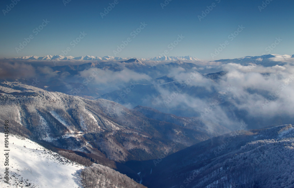 Forested Revucka dolina valley below Donovaly between Velka Fatra and Nizke Tatry ranges with low clouds and snow covered jagged Zapadne and Vysoke Tatry peaks on horizon Carpathians Slovakia Europe