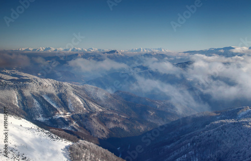 Forested Revucka dolina valley below Donovaly between Velka Fatra and Nizke Tatry ranges with low clouds and snow covered jagged Zapadne and Vysoke Tatry peaks on horizon Carpathians Slovakia Europe © nogreenabove2k