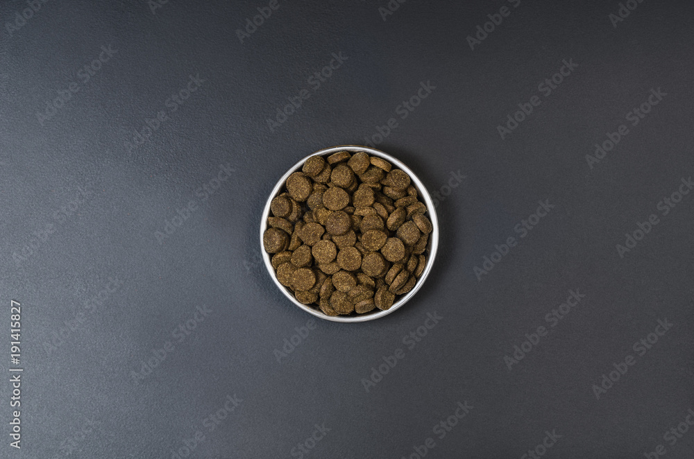 Fototapeta premium Dry dog pet food in bowl on blach chalkboard background top view. Pet feeding concept backgrounds with copy space. Photograph taken from above.