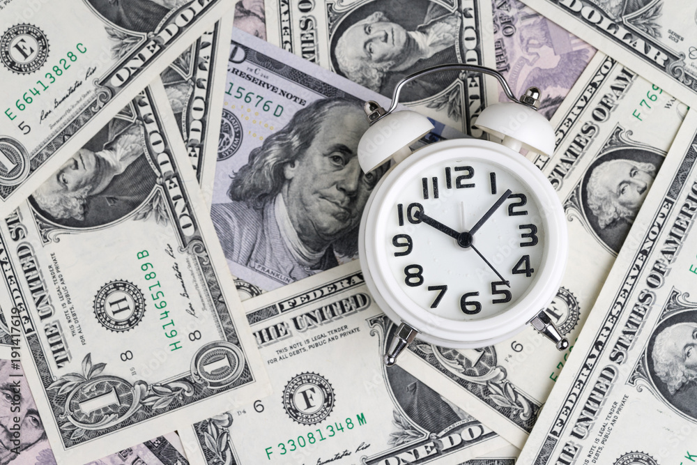 White alarm clock on US dollar banknotes as time for money awareness or compound interest of investment concept White alarm clock on US dollar banknotes as time for money awareness or compound interest of investment concept
