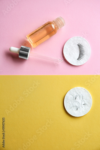 Bottle of oil and cotton pads with false eyelashes on color background