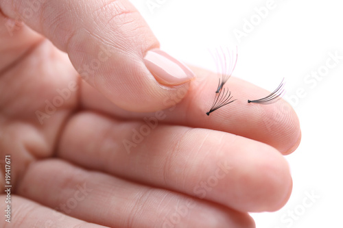 Woman holding false eyelashes on light background, closeup