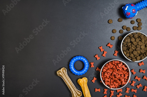 Dry dog pet food in bowl and accessories on blach chalkboard background top view. Pet feeding concept backgrounds with copy space. Photograph taken from above.