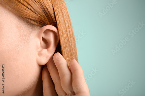 Young woman with hearing problem on color background, closeup photo