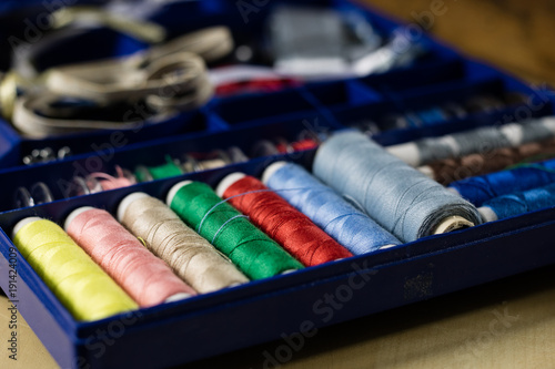 Garment accessories spread on a light wooden table. Threads, scissors and sewing needles in a tailoring workshop.