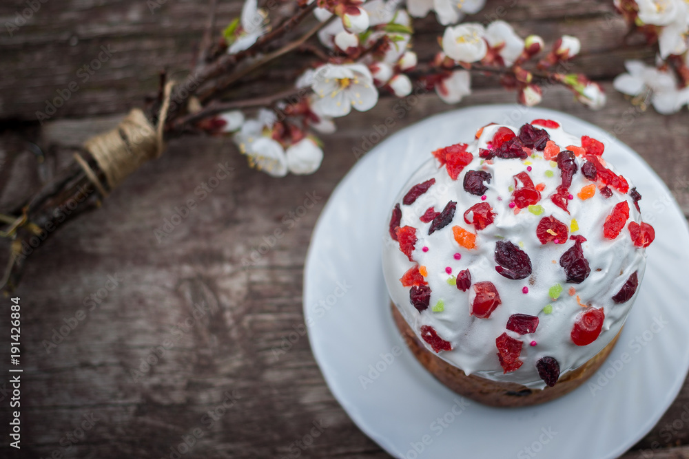 Beautiful Easter cake stands on a wooden texture surface, near lies flowering apricot. place under text Beautiful Easter cake stands on a wooden texture surface, near lies flowering apricot. place under text