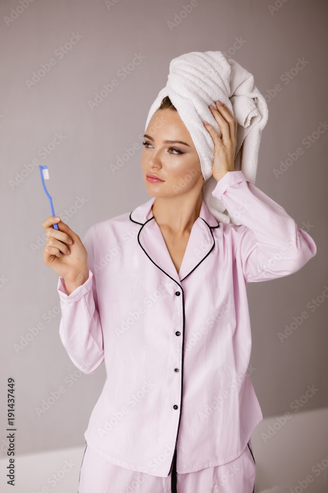 Portrait of beautiful lady in pink sleepwear standing with towel on her head and toothbrush in hand while dreamily looking aside isolated Portrait of beautiful lady in pink sleepwear standing with towel on her head and toothbrush in hand while dreamily looking aside isolated