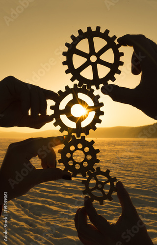 four hands are holding the gears against the sunset. teamwork. harmonious work.