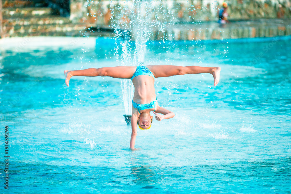 Happy little girl enjoy vacation in the swimming pool. Sporty kid making cartwheel on the edge of pool