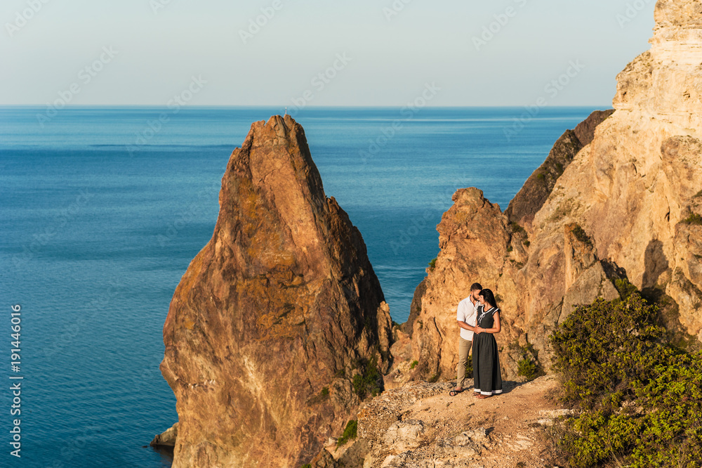 Guy and girl at the sea hugging on the edge of the cliff. A guy proposes to a girl. Honeymoon in the mountains. Man and woman traveling. Wedding. Journey. Love. Newlyweds resting on the sea. Сouple