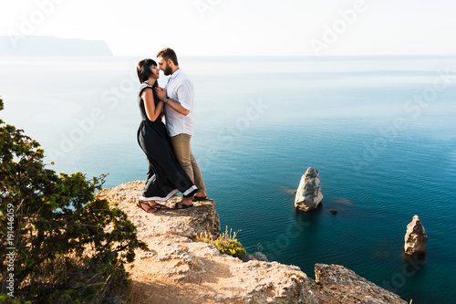 Couple in love at dawn by the sea. Honeymoon. Honeymoon trip. Boy and girl at the sea. Man and woman traveling. Couple hugs. Couple kissing. Newly married couple. Wedding travel. Holiday romance