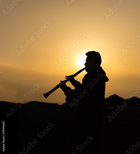 An unidentified man plays clarinet at sunset