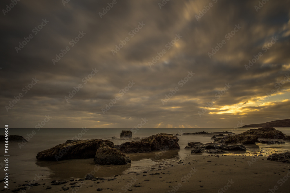 Obraz premium Beach on a Canarian island with dark clouds and big lava mountains at sunset