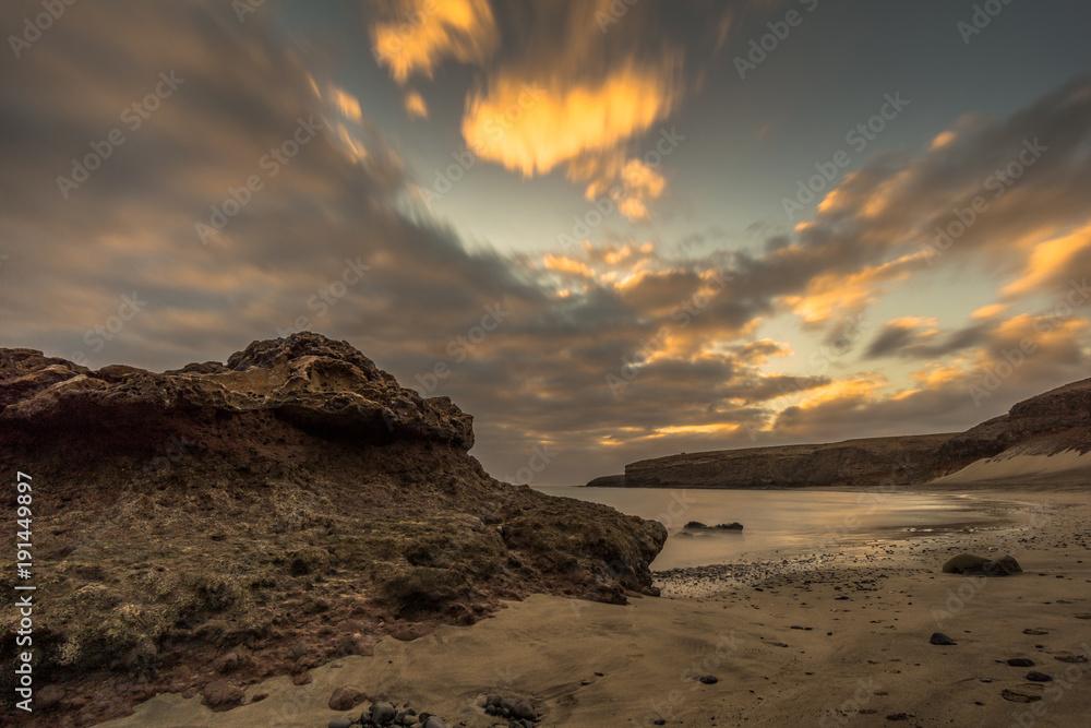 Beach on a Canarian island with dark clouds and big lava mountains at sunset