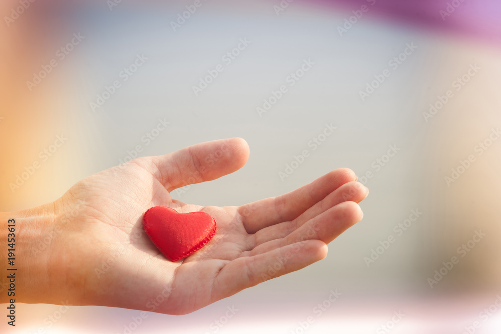 Red fabric heart lay on palm of hand with sea on background. Valentine day. Purple pink blurred