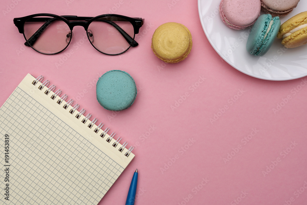 Obraz premium Woman's flat lay workplace with glasses, pen, notebook and pastel macaroons. Place for text.