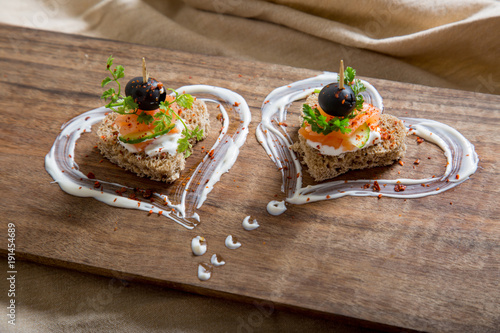 Appetizer canape with salmon fish, cheese and olive on a small loaf of bread, closeup