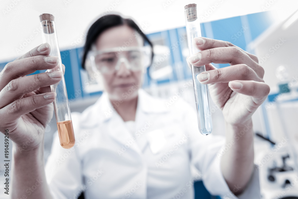 Let me see. Selective focus on two test tubes containing chemical liquids held by a mature lady in a labcoat standing in a laboratory and examining the liquids. Let me see. Selective focus on two test tubes containing chemical liquids held by a mature lady in a labcoat standing in a laboratory and examining the liquids.